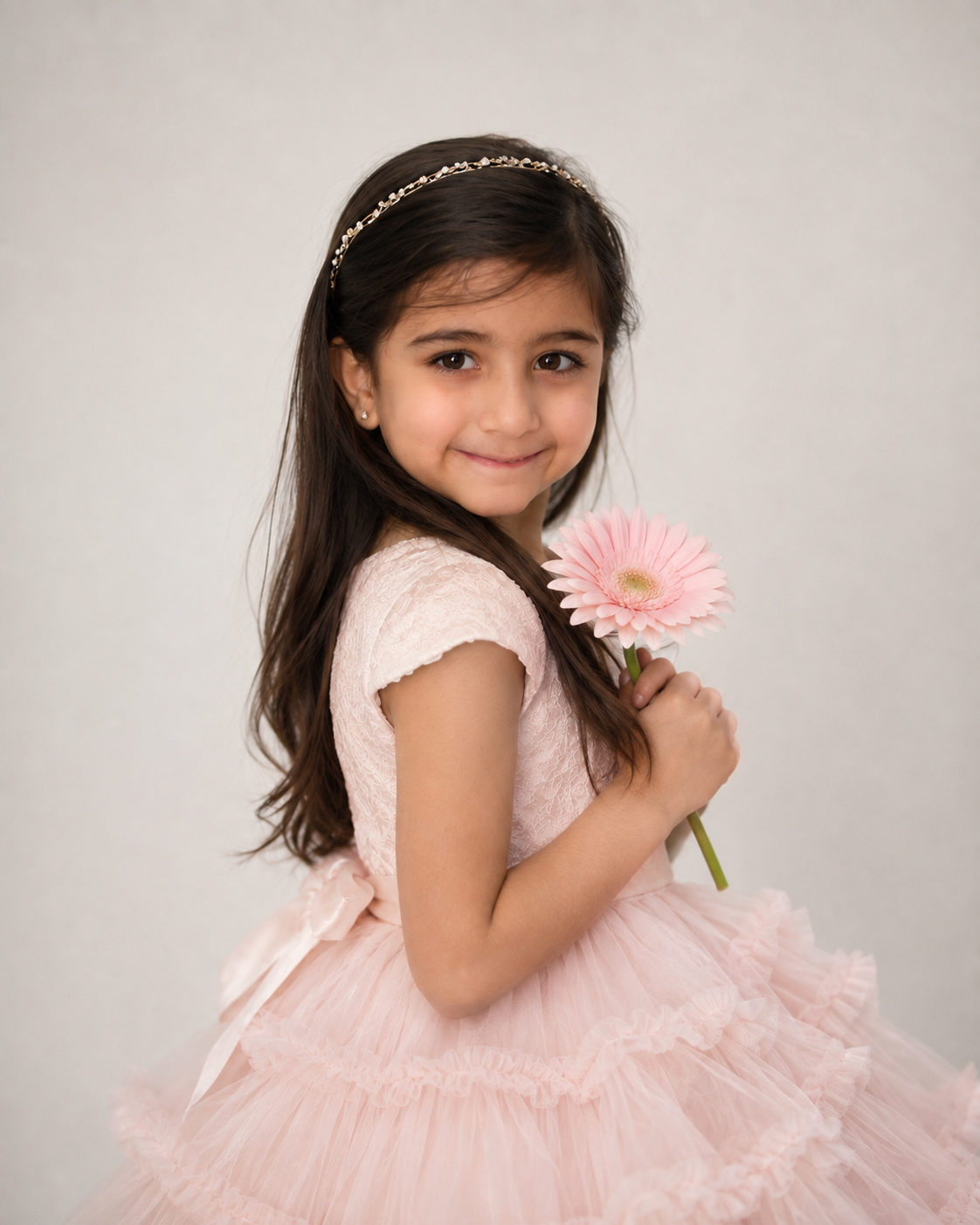 Young girl in a blush ruffled dress holding a pink gerbera daisy in the North York studio